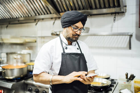 Indian chef using smartphone in restaurant kitchen - OCMF01042