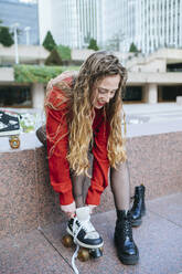 Young woman putting on roller skates in the city - KIJF02896