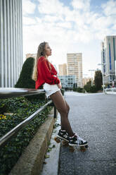 Young woman on roller skates leaning against railing in the city - KIJF02922