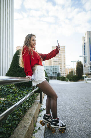 Smiling young woman on roller skates taking a selfie in the city stock photo