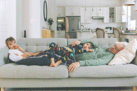 Vater und zwei Kinder entspannen sich auf der Couch, lizenzfreies Stockfoto