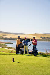 Männliche Golffreunde unterhalten sich auf einem sonnigen Golfplatz am See - CAIF23865