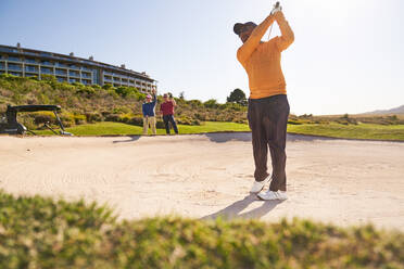 Männlicher Golfer bei einem Schlag aus einem sonnigen Bunker - CAIF23870