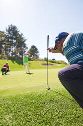 Männlicher Golfer bereitet sich auf einen Schlag auf dem sonnigen Putting Green vor - CAIF23873