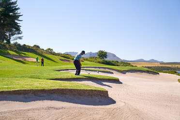 Männlicher Golfer bei einem Schlag über dem sonnigen Sandloch - CAIF23874