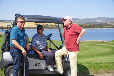 Glückliche reife männliche Golfer unterhalten sich am sonnigen Golfwagen - CAIF23885