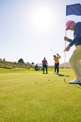 Männlicher Golfer beim Putten zum Loch auf dem sonnigen Golfplatz Putting Green - CAIF23888