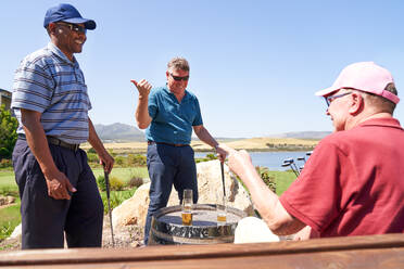 Glückliche männliche Golfer, die sich auf der Terrasse des Clubhauses unterhalten und Bier trinken - CAIF23892