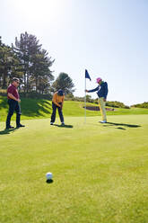 Männlicher Golfer beim Einlochen auf dem sonnigen Golfplatz Putting Green - CAIF23893