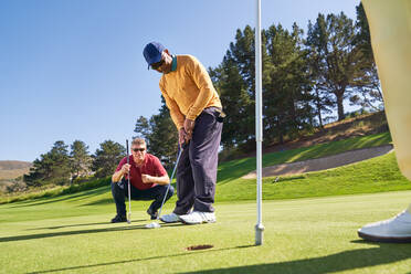 Männlicher Golfer beim Einlochen auf dem sonnigen Golfplatz Putting Green - CAIF23895