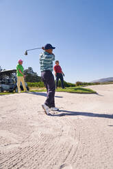 Männlicher Golfer bei einem Schlag aus einem sonnigen Golfbunker - CAIF23896