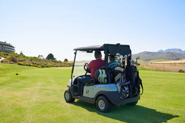 Männliche Golfer fahren Golfwagen auf dem sonnigen Grün des Golfplatzes - CAIF23903