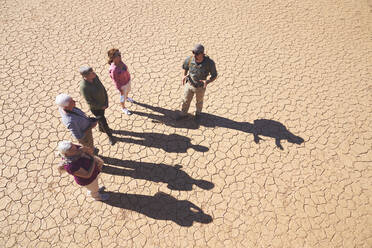 Safari-Reiseleiter im Gespräch mit der Gruppe auf der sonnigen, rissigen Erde - CAIF23910