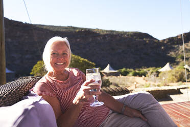 Portrait happy senior woman drinking water on sunny safari hotel patio - CAIF23934