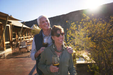 Happy senior couple drinking iced tea on sunny safari lodge balcony - CAIF23936