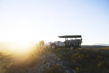 Safari-Gruppe außerhalb des Geländewagens auf einem ruhigen Hügel bei Sonnenaufgang - CAIF23940