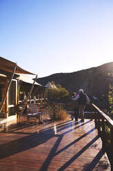 Zärtliches älteres Paar, das sich auf dem sonnigen Balkon einer Safari-Lodge umarmt - CAIF23954