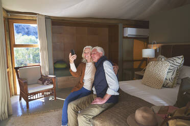 Glückliches älteres Paar macht Selfie mit Fotohandy im Hotelzimmer - CAIF23960