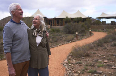 Glückliches Seniorenpaar auf dem Fußweg vor der Safari-Lodge - CAIF23981