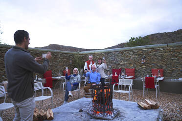 Ältere Freunde mit Wein posieren für ein Foto an der Feuerstelle auf der Terrasse - CAIF23988