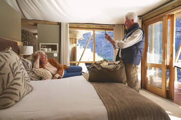 Älterer Mann mit Fotohandy, der seine Frau auf dem Hotelbett fotografiert - CAIF23993