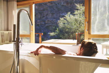 Serene woman taking a bath in sunny hotel room - CAIF24000