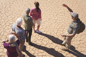 Safari-Reiseleiter im Gespräch mit der Gruppe auf der sonnigen, rissigen Erde - CAIF24009