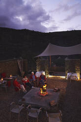 Senior friends relaxing at fire pit on hotel patio - CAIF24013