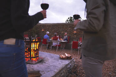 Paar und ältere Freunde speisen und trinken Wein auf einer Terrasse mit Feuerstelle - CAIF24017