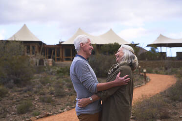 Zärtliches älteres Paar, das sich vor einem Safari-Lodge-Hotel umarmt - CAIF24026