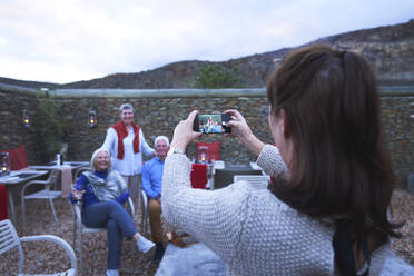 Frau mit Fotohandy fotografiert ältere Freunde auf der Hotelterrasse - CAIF24032