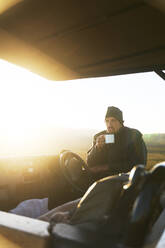 Safari-Führer trinkt Tee am Geländewagen bei Sonnenaufgang - CAIF24044