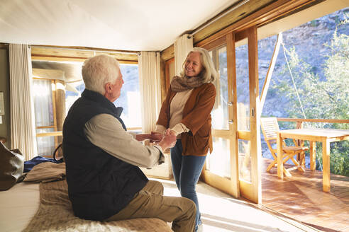 Glückliches älteres Paar, das sich im Hotelzimmer einer Safari-Lodge an den Händen hält - CAIF24048
