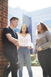 College students talking outside sunny building - CAIF24089