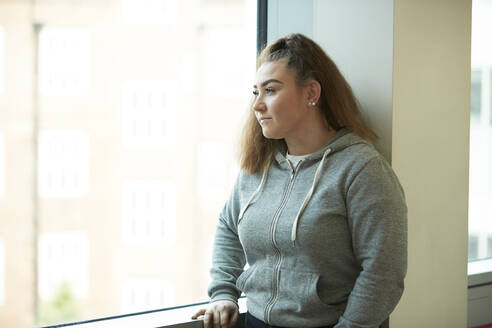 Nachdenkliches Teenager-Mädchen schaut aus dem Fenster - CAIF24112