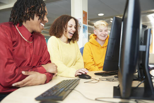 Glückliche College-Studenten, die gemeinsam am Computer in der Bibliothek lernen - CAIF24144