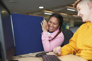 Glückliche junge Studentinnen lachen am Computer in der Bibliothek - CAIF24150