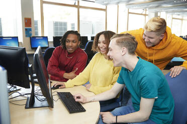 Happy young college students using computer together in library - CAIF24151