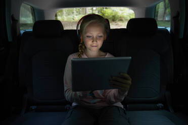 Mädchen mit Kopfhörern und digitalem Tablet auf dem Rücksitz eines Autos - CAIF24251