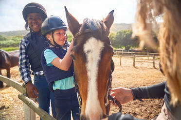 Happy girls learning horseback riding in sunny paddock - CAIF24259