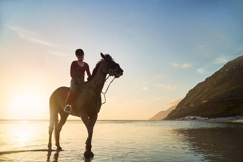 Porträt junge Frau Reiten auf ruhigen Sonnenuntergang Ozean Strand - CAIF24260