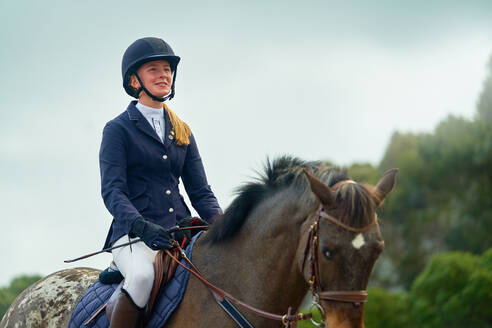 Selbstbewusst lächelndes Teenager-Mädchen reitet auf einem Pferd - CAIF24267