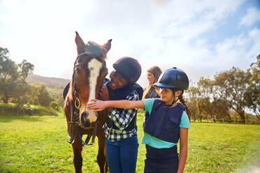 Glückliche Mädchen streicheln Pferd in sonnigen ländlichen Paddock - CAIF24268