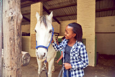Happy girl petting horse outside stables - CAIF24269