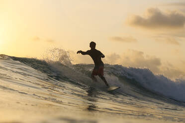 Junger Mann, der bei Sonnenuntergang surft - CAVF74870