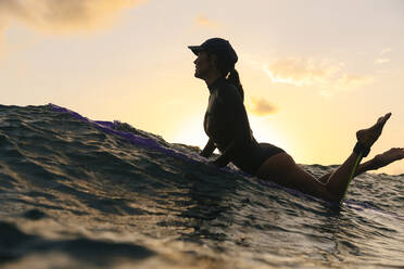 Weibliche Surferin auf dem Surfbrett liegend am Abend - CAVF74874