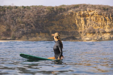 Glückliche Frau sitzt auf einem Surfbrett im Meer - CAVF74876