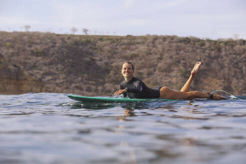 Glückliche Frau sitzt auf einem Surfbrett im Meer - CAVF74877