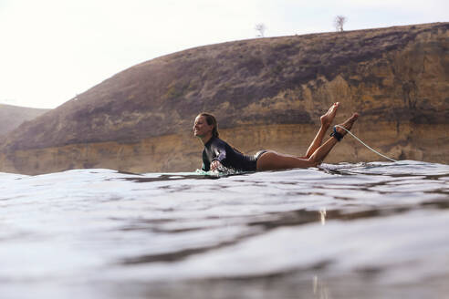 Glückliche Frau sitzt auf einem Surfbrett im Meer - CAVF74878