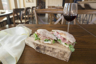 Seitenansicht eines italienischen Prosciutto-Sandwichs auf einem Brett und ein Glas Wein - CAVF74945